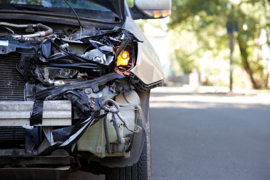 Close up of wrecked car front smashed quiet urban street in background sunny day